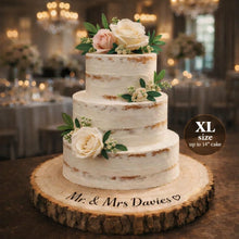 Load image into Gallery viewer, May include: A three-tiered wedding cake with white frosting and floral decorations, including roses and greenery. The cake sits on a rustic wooden cake stand. Text on the stand reads "Mr. & Mrs Davies". The image also includes text that reads "XL size up to 35.5cm cake".