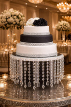 Load image into Gallery viewer, May include: A three-tiered wedding cake with white and black icing, decorated with crystal detailing and topped with white and black roses. The cake is on a mirrored stand with hanging crystal strands.
