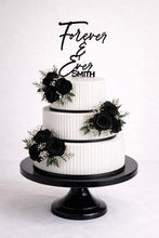 Load image into Gallery viewer, May include: A three-tiered white wedding cake with black rose floral arrangements and a black cake stand. The cake is decorated with black ribbon and a topper that reads "Forever &amp; Ever Smith."
